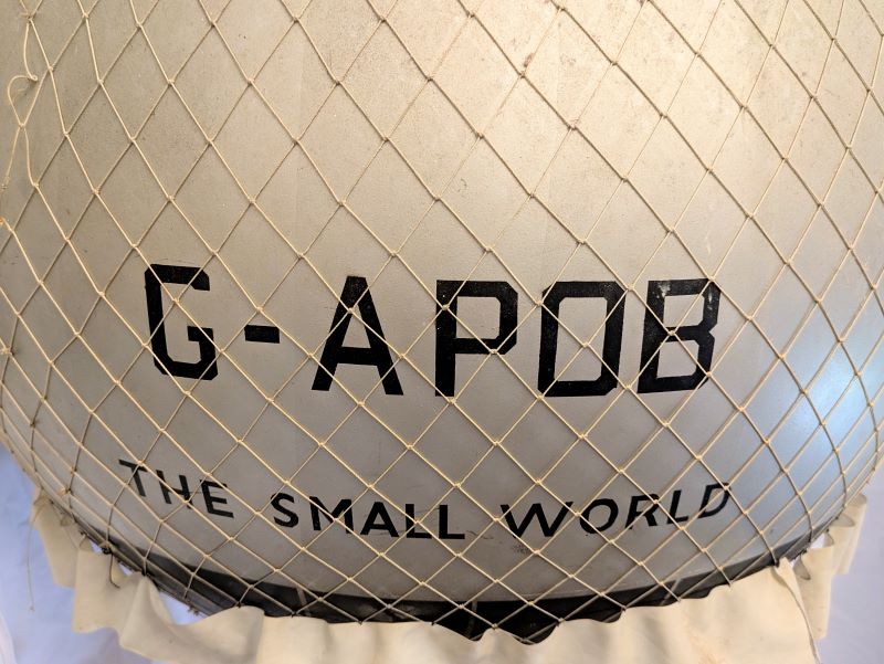 Close up picture of a section of silver coloured balloon bearing the registration G-APOB and the name The Small word and showing the perfect net constructed with delicate thin thread and perfect knots